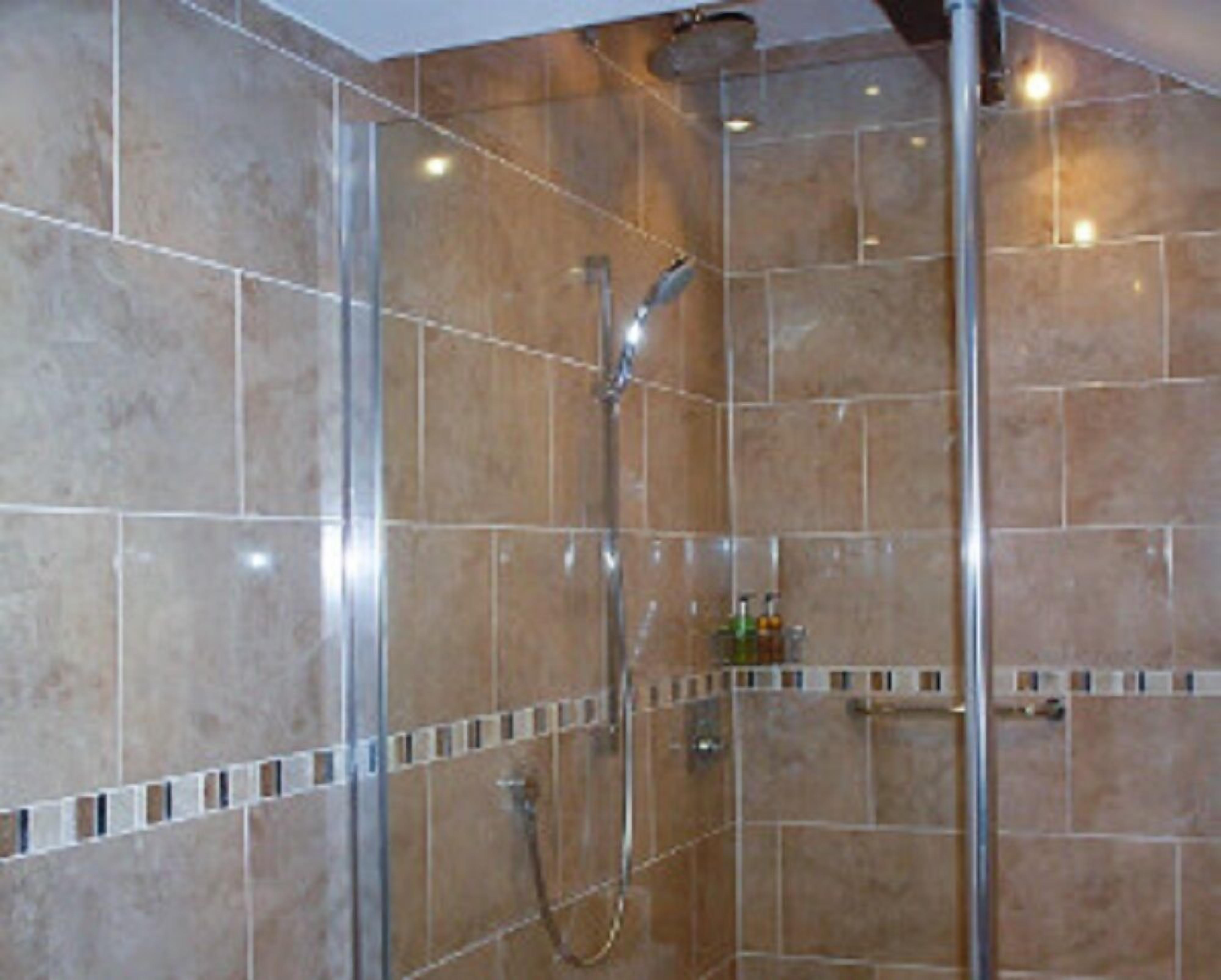 A shower with a glass door, tiled walls, and a handheld showerhead.