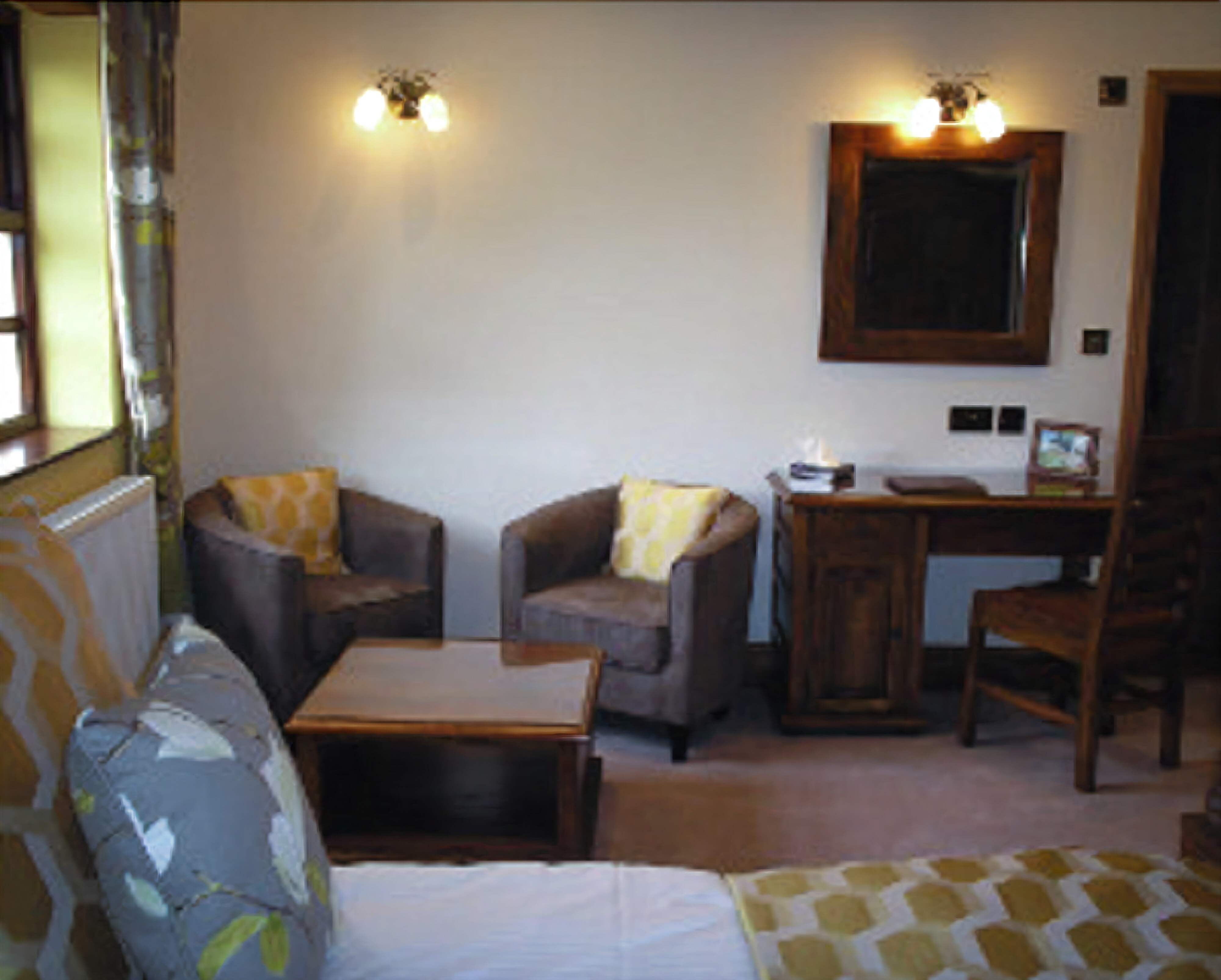 A cozy room with a bed, two armchairs, a small table, a desk, and a mirror on the wall.