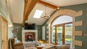 A living room with a fireplace, wooden beams, a sofa, and a large window. - GreenGrove Country House B&B (Skipton)