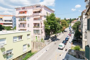 A multi-story building with balconies, a street with parked cars, and a clear sky. - Capital Apartments (Split)