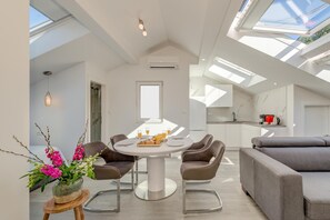 A modern interior with a round dining table, grey sofas, and a skylight. - Capital Apartments (Split)