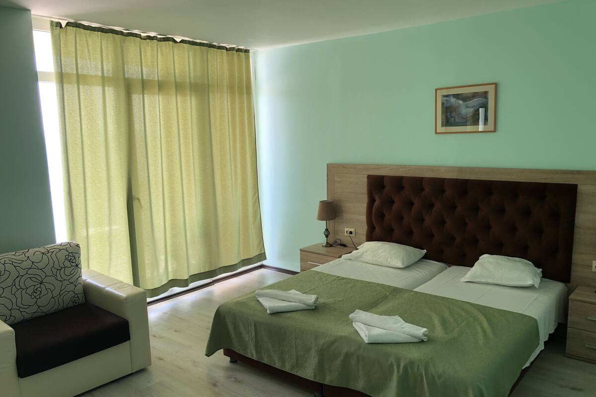 A hotel room with a bed, a nightstand, a lamp, a chair, and a window with curtains.