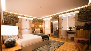A bedroom with a bed, a desk, and a chair. There is a stone wall and a wooden floor. - Quinta da Pousada (Santa Marta de Penaguião)