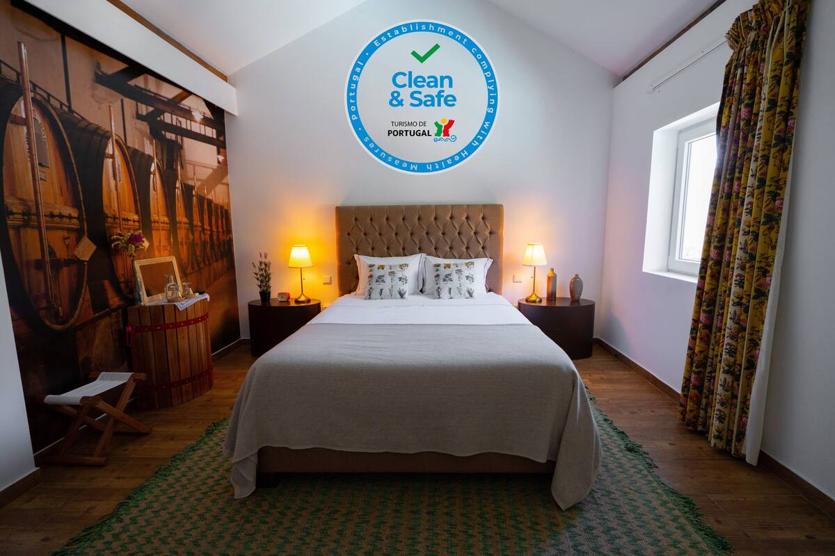 Une chambre d’hôtel avec un lit, deux tables de chevet avec des lampes, une fresque murale, une fenêtre avec des rideaux et un panneau circulaire au-dessus du lit.
