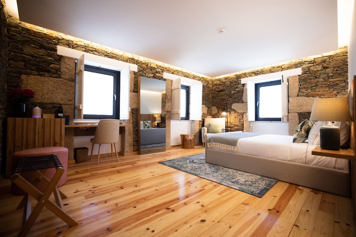 Une chambre avec des murs en pierre, un plancher en bois, un lit, un bureau et une chaise.