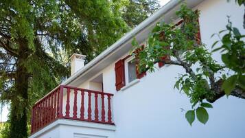 Un edificio blanco con un balcón rojo y una ventana con persianas rojas.