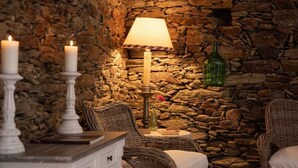 A cozy room with wicker furniture, a stone wall, a table with candles, a lamp, and a vase with flowers. - Quinta da Pousada (Santa Marta de Penaguião)