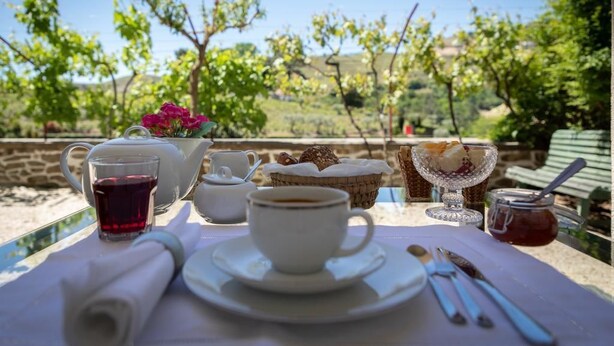 A table set with a cup of coffee, a glass of tea, a teapot, a basket of bread, and a jar of jam. - Quinta da Pousada (Santa Marta de Penaguião)