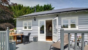 Et hus med en terrasse, et spiseområde med bord og stole, og en dør der fører ind.
