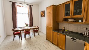A kitchen with wooden cabinets, a dishwasher, a dining table with chairs, and a window with curtains. - Central Retro Apartment (Prague)