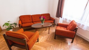 A room with a herringbone wooden floor, a sofa, two armchairs, a small round table, and a potted plant. - Central Retro Apartment (Prague)