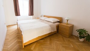 A bedroom with a wooden bed, a bedside table with a lamp, a nightstand, and a potted plant. - Central Retro Apartment (Prague)