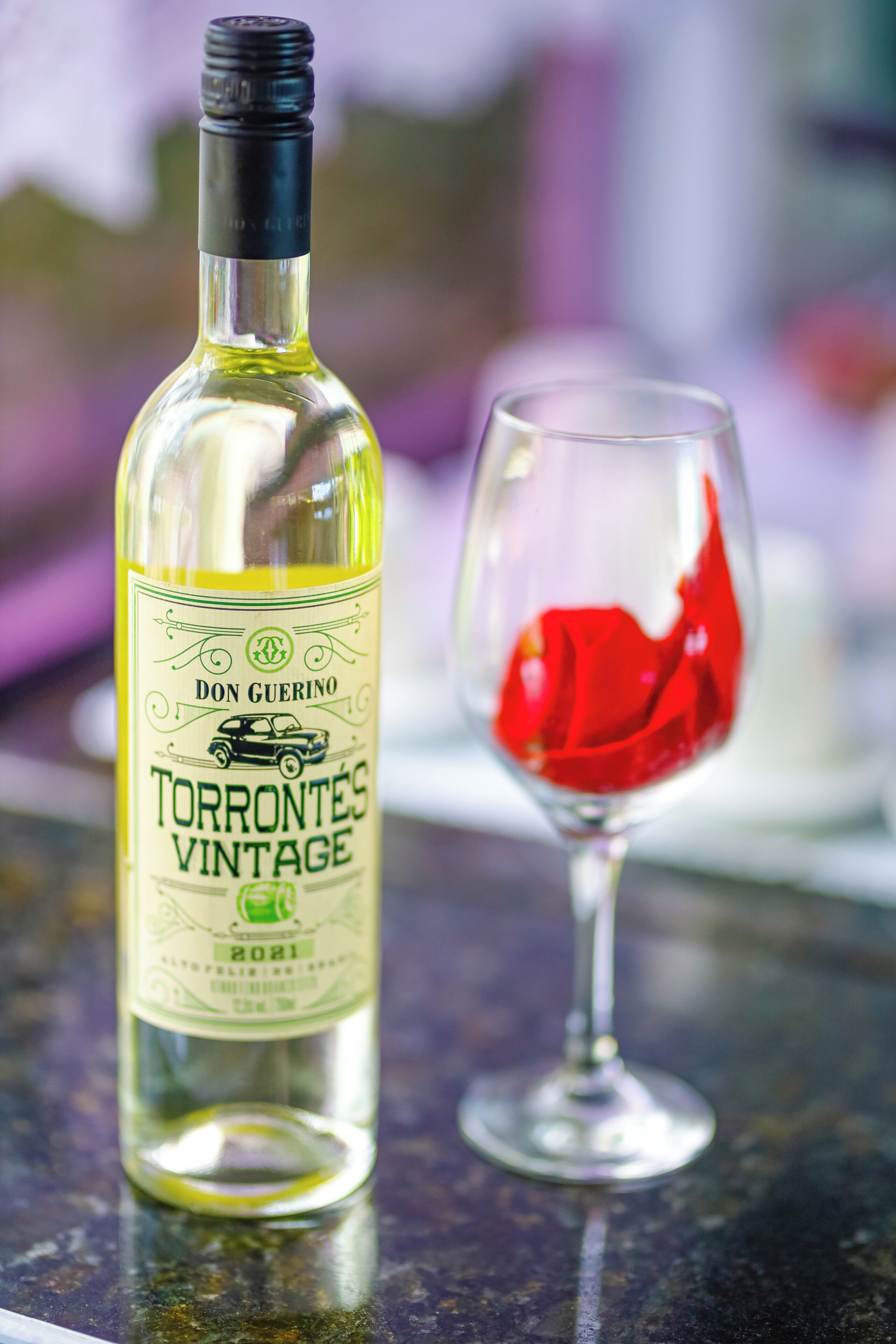 A bottle of Torrontes vintage wine and an empty wine glass on a table.