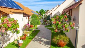 A pathway leading through a courtyard with solar panels, potted plants, and small buildings with tiled roofs. - Pousada Polymar (Maragogi)