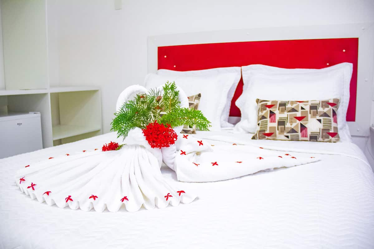 A neatly made bed with white linens and a decorative arrangement of white towels and red flowers.