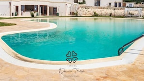 A swimming pool with a clear blue water, surrounded by a stone deck and a white building with a balcony.