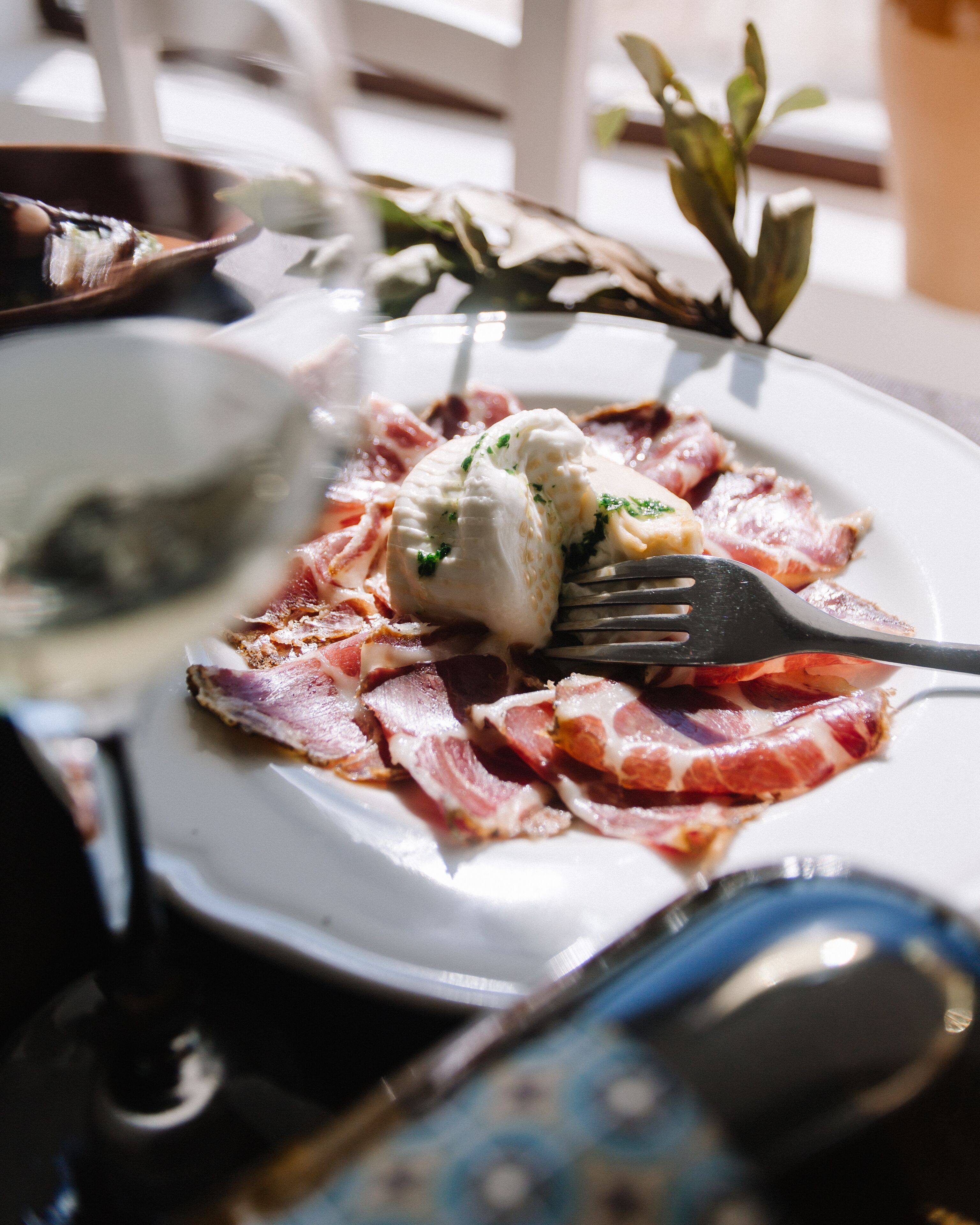 A plate with a piece of white cheese, bacon, and a fork.