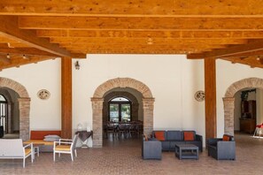 An open-plan living area with brick flooring, wooden beams, and a dining area with tables and chairs.