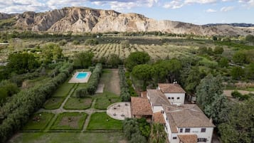 A villa with a swimming pool, surrounded by terraced gardens and a mountainous backdrop.