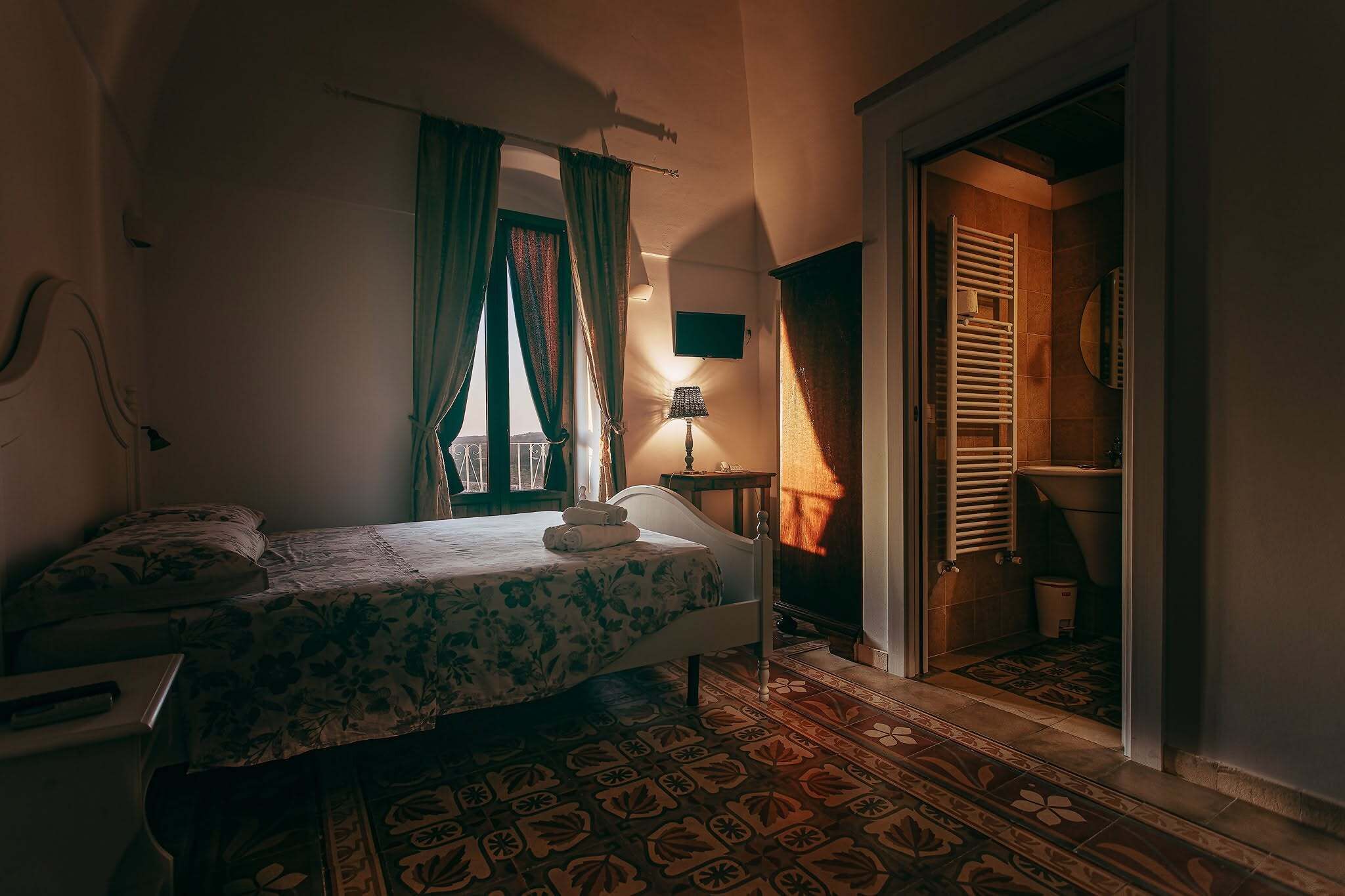 Un dormitorio con cama, mesita de noche, lámpara y vistas a un balcón.