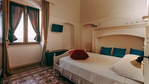 A hotel room with a bed, a TV, a desk, and a patterned floor.