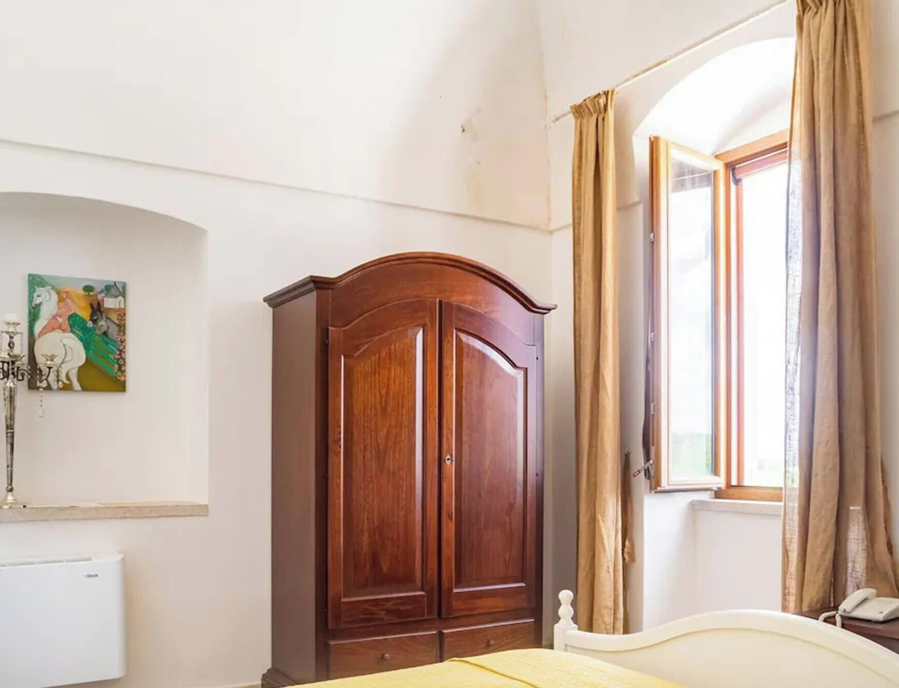 Una camera da letto con un letto, un armadio, un termosifone, un quadro e una finestra con tende.