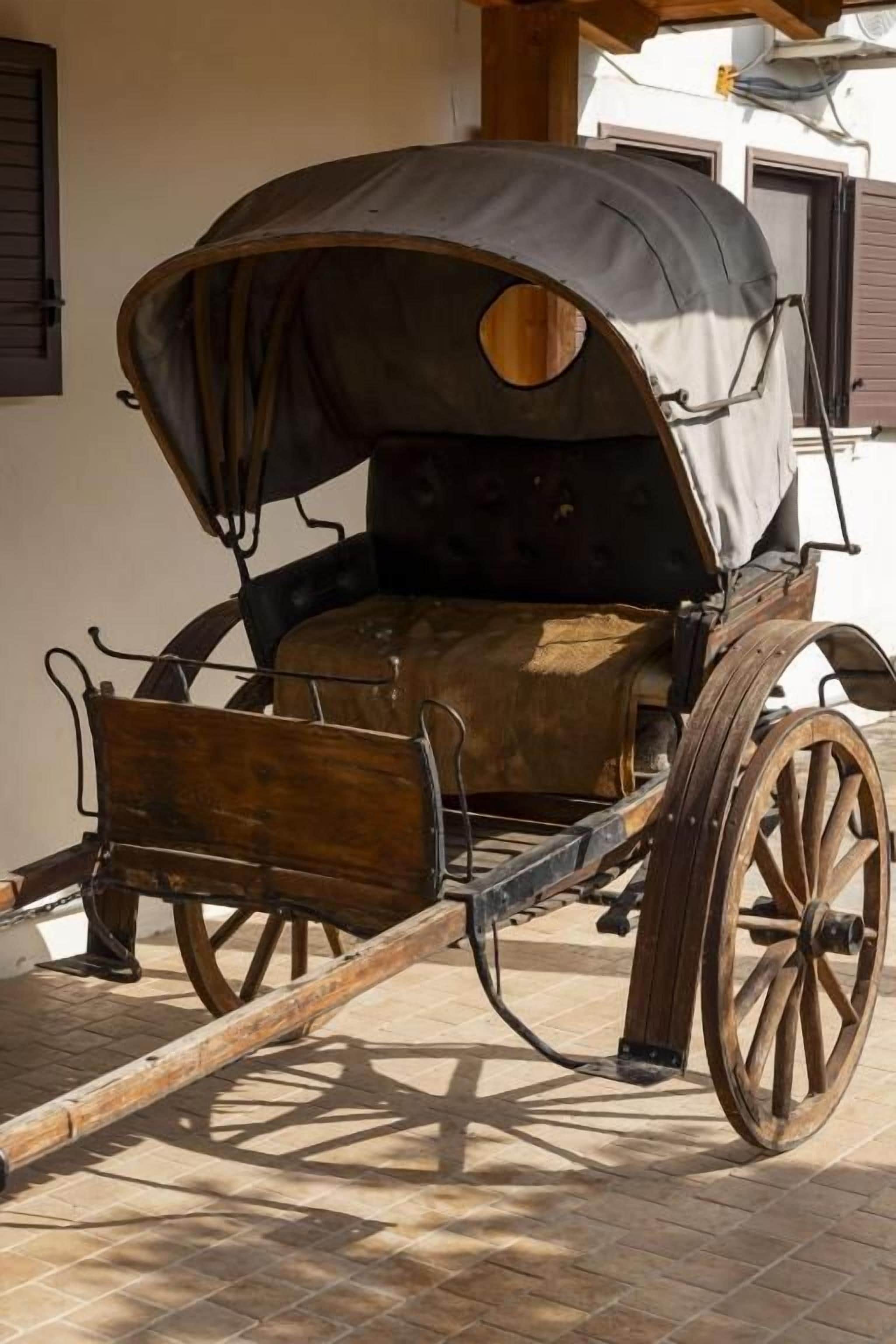 A vintage carriage with a covered seat and wooden wheels.