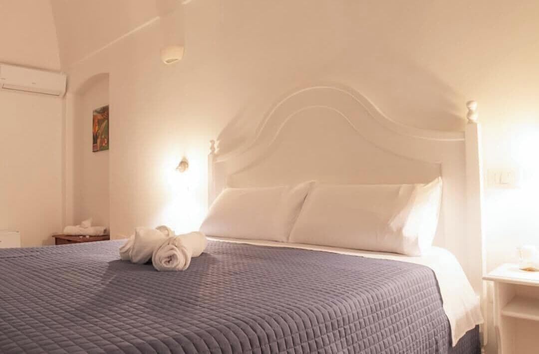 Een net opgemaakt bed met een gewatteerde deken, een wit hoofdbord en een klein nachtkastje met een lamp.