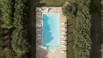 Vista aérea de una piscina rectangular rodeada de sillas de descanso y una terraza de piedra.