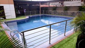 Piscina com guarda-corpo de metal, rodeada por relva artificial e plantas de palmeira.