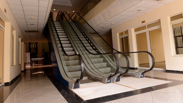 Escalator interno em edifício com piso ladrilhado e teto com iluminação embutida.