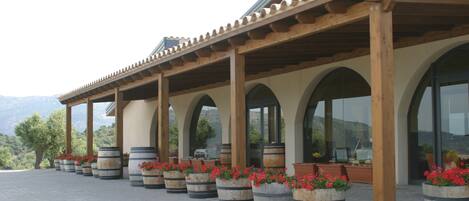 Un espacio al aire libre cubierto con columnas y arcos de madera, plantas en macetas y vistas a las montañas.