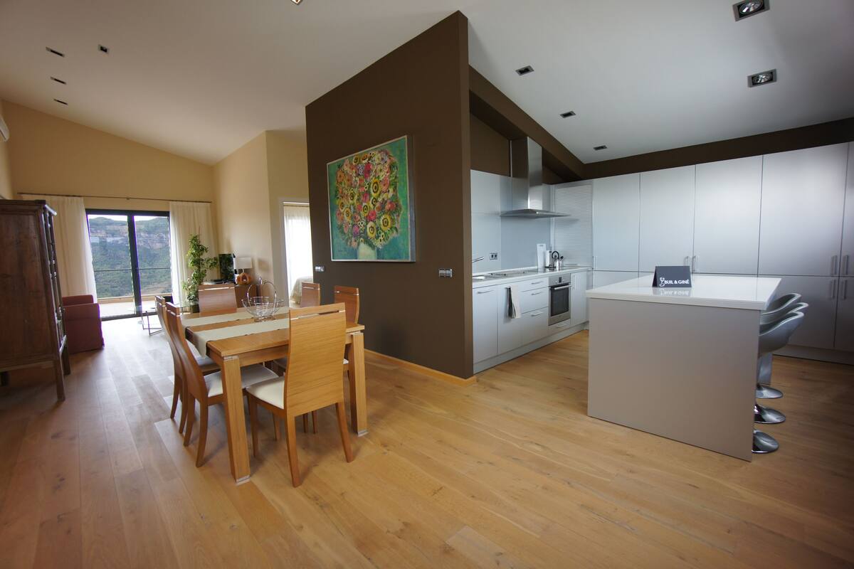 Una cocina moderna con comedor, piso de madera y un amplio ventanal con cortinas.