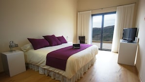 Un dormitorio con cama, mesita de noche, televisor y vistas al exterior.