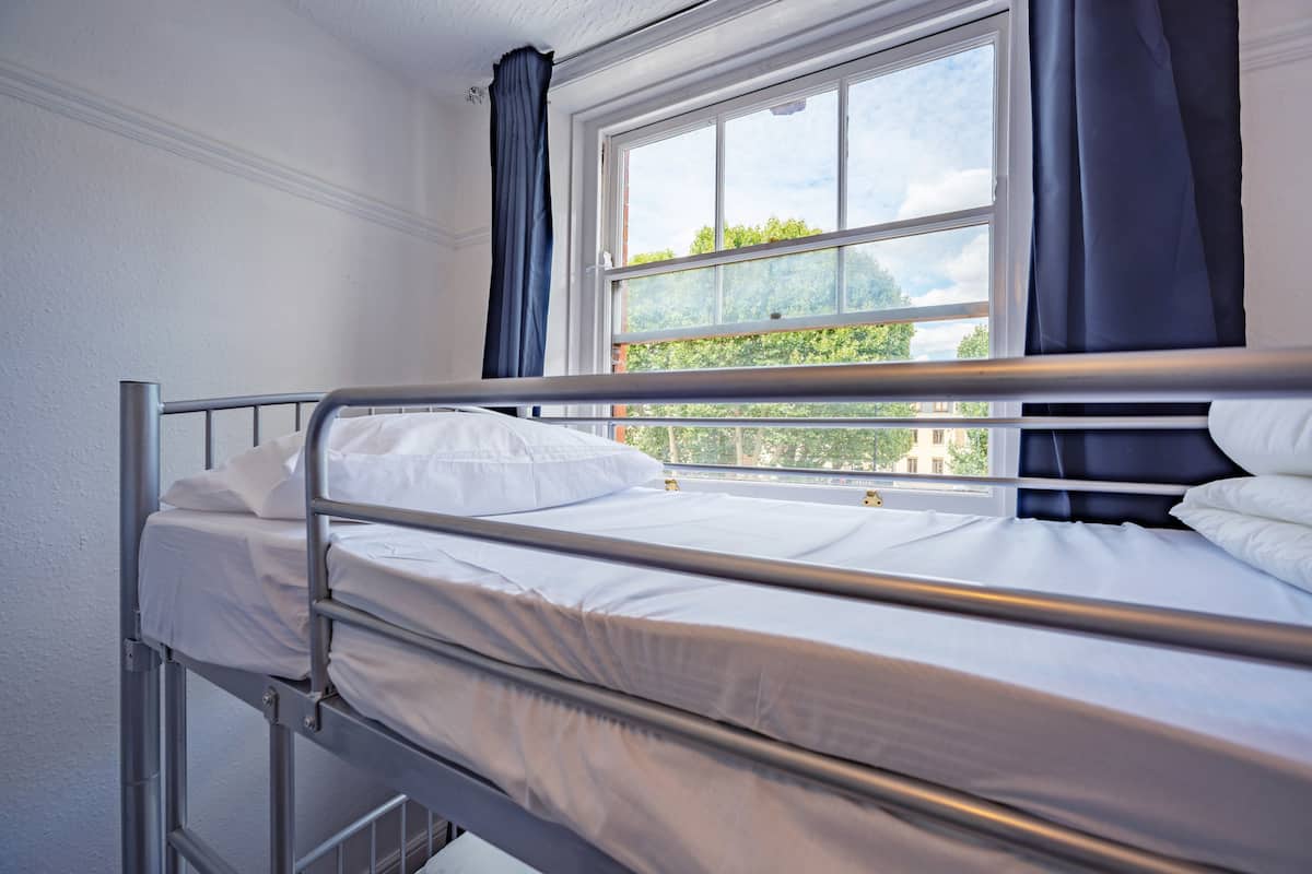 Una cama litera con ropa de cama blanca y una ventana con cortinas.
