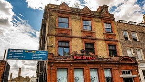 A historic building with a sign for 'Red Dragon' and a signboard listing various businesses. - Mile End Beds - Hostel (London)