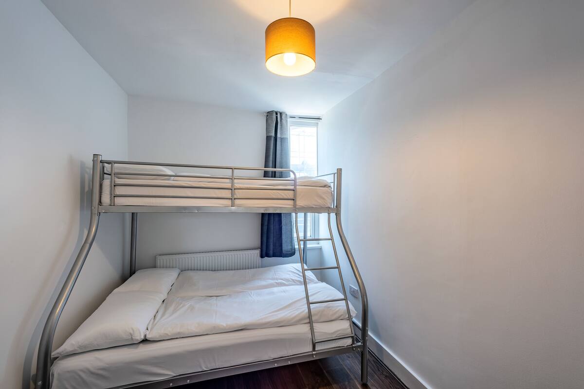 Una cama litera con estructura metálica, ropa de cama blanca y una lámpara colgante.