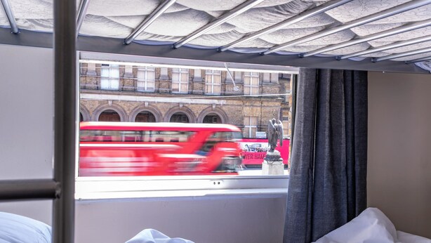 A room with a bed, a window, and a view of a red bus on the street. - Mile End Beds - Hostel (London)