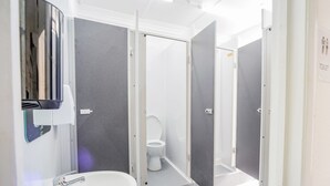 A modern bathroom with a sink, mirror, and two toilets. - Mile End Beds - Hostel (London)