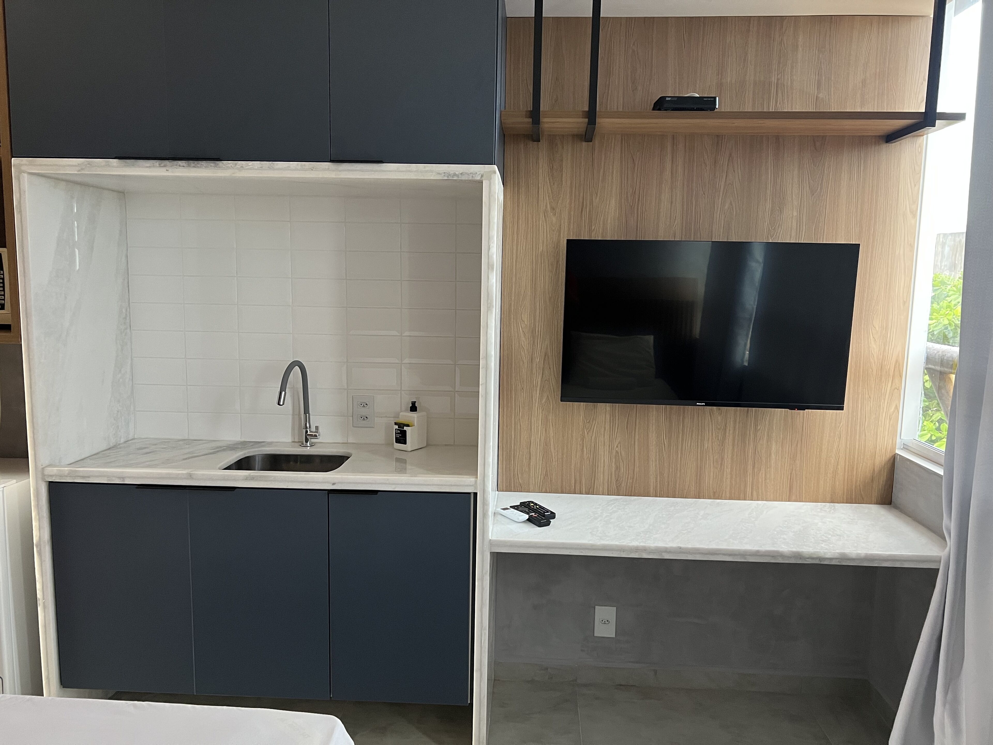 Una cucina moderna con lavello integrato, TV a schermo piatto montata su una parete in legno e un piccolo bancone.