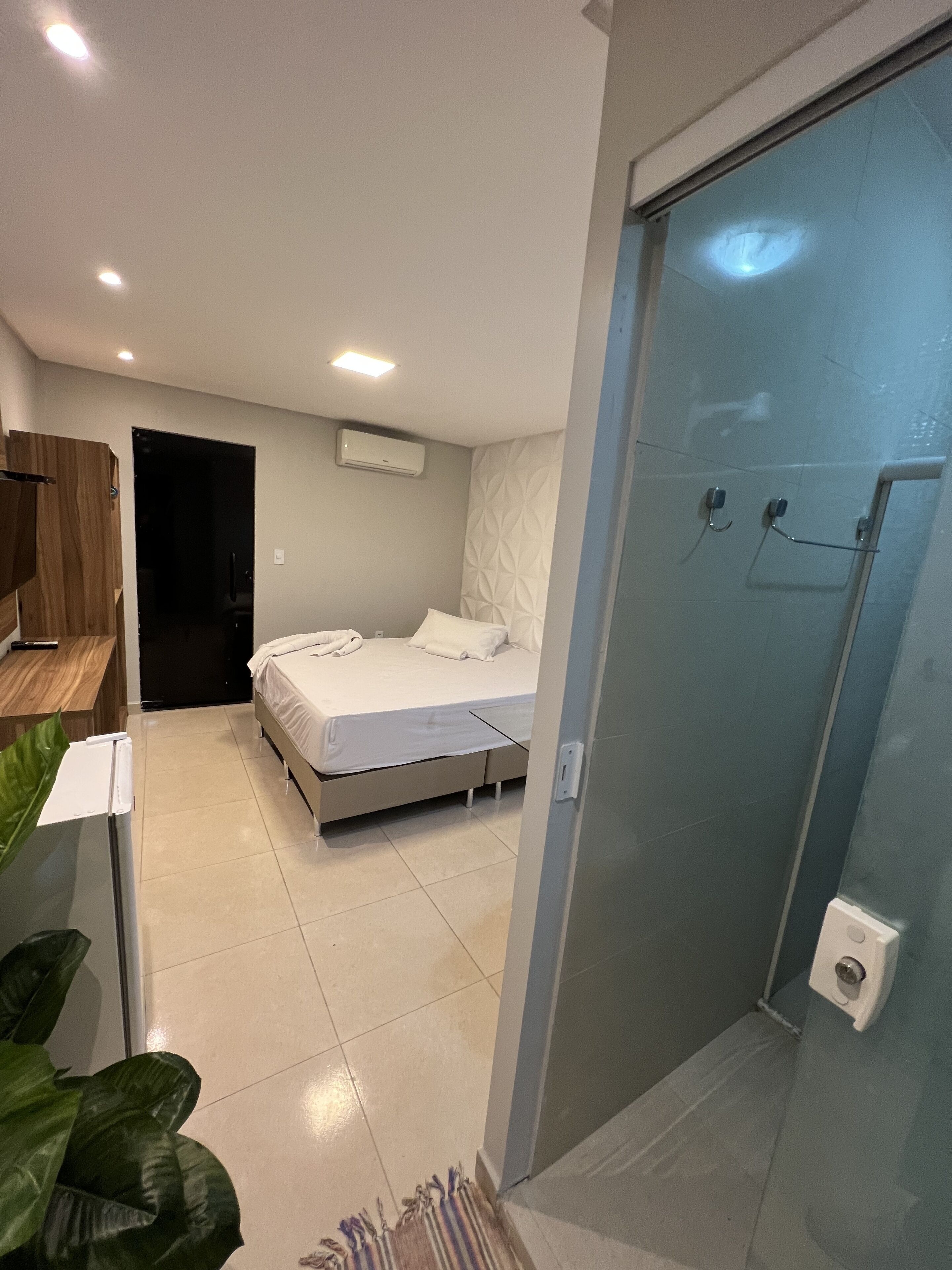 A modern bedroom with a bed, a shower area, and a wooden desk.