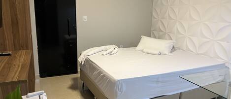 A modern hotel room with a bed, a glass table, a wooden wardrobe, and an air conditioning unit.