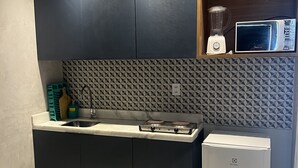 A modern kitchen with dark cabinets, a built-in microwave, a blender, and a compact refrigerator. - Pousada Marbello (Maragogi)