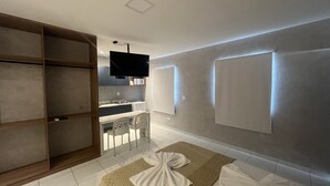 A modern hotel room with a large wardrobe, a flat-screen TV, a microwave, a small kitchen area, and a bed with a patterned blanket. - Pousada Marbello (Maragogi)