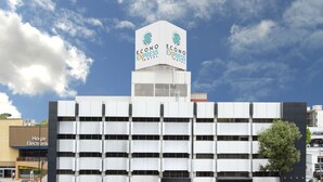 Un hotel moderno con un letrero llamativo en la azotea, varios pisos y un estacionamiento.