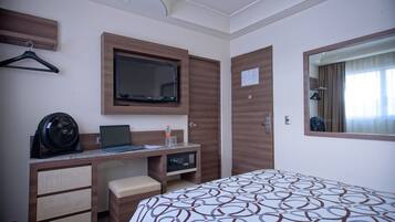 A hotel room with a bed, a desk with a laptop, a television, and a mirror.
