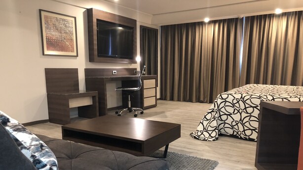 Una habitación de hotel moderna con televisor de pantalla plana, un escritorio, un sofá confortable y una cama con ropa de cama estampada.