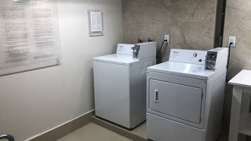Uma lavanderia com duas máquinas de lavar e secar Whirlpool, uma placa com normas de lavanderia e uma parede de mármore.