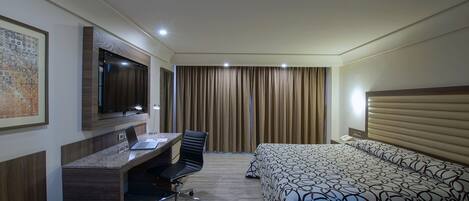 A hotel room with a desk, chair, bed, and a large window with curtains.