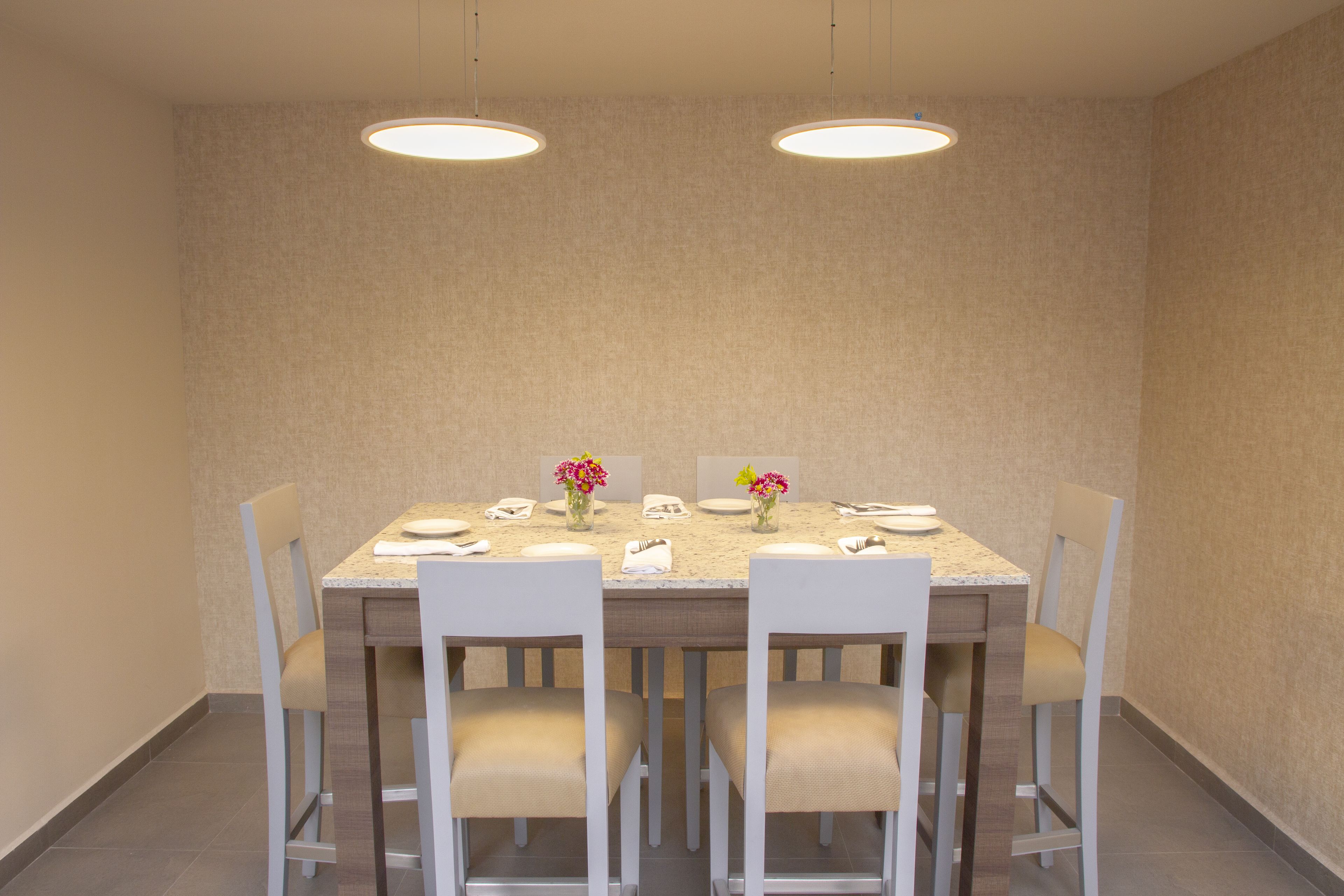 A dining area with a rectangular table, six chairs, two pendant lights, and floral centerpieces.